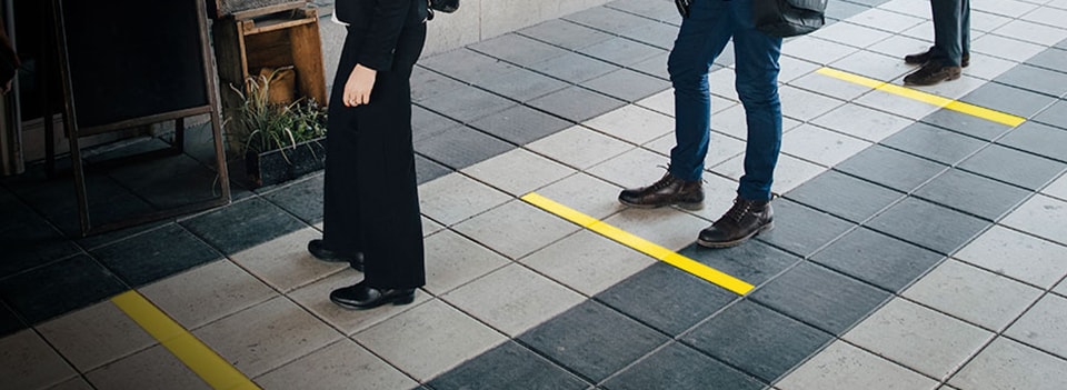 People practicing social distancing by queueing within the yellow floor tape