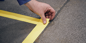 A hand applying 3M™ Floor & Safety Marking Tape on the floor